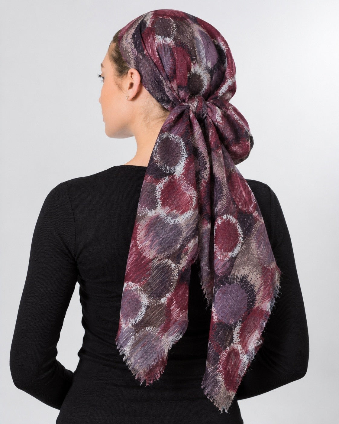 Collected NYC abstract circle print headscarf in burgundy, plum, and grey with frayed edges worn as a head wrap.